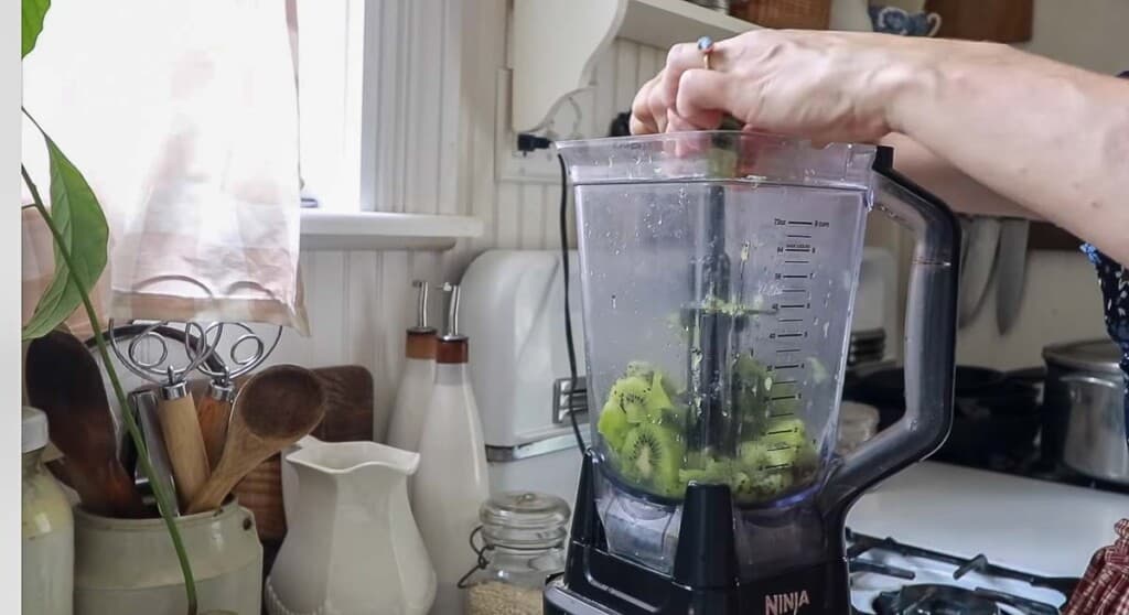 women squeezing a lime into a blender with kiwi in the blender