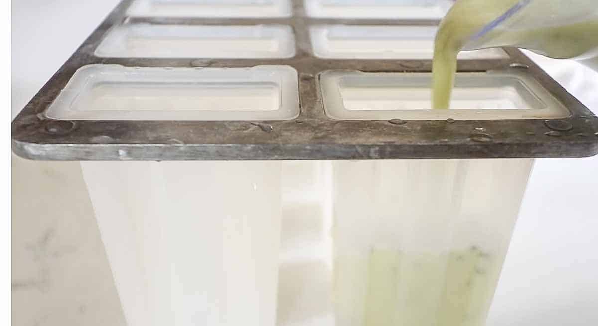 pouring kiwi lime popsicle mixture into popsicle mold