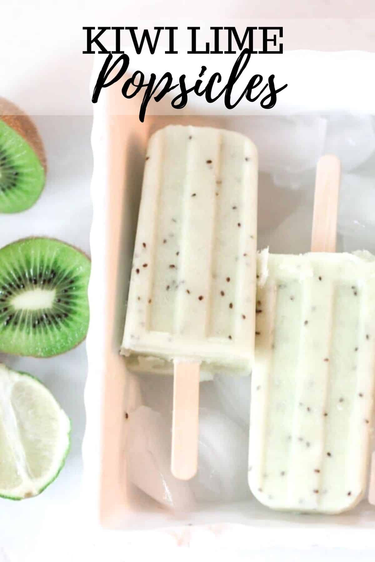 two kiwi lime popsicles in a white dish with ice. Halved kiwis and a lime sit to the left of the dish