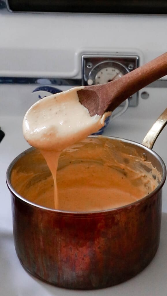 pumpkin pasta sauce in a copped pot with a wooden spoon scooping out the sauce and allowing it to drip back into the pan