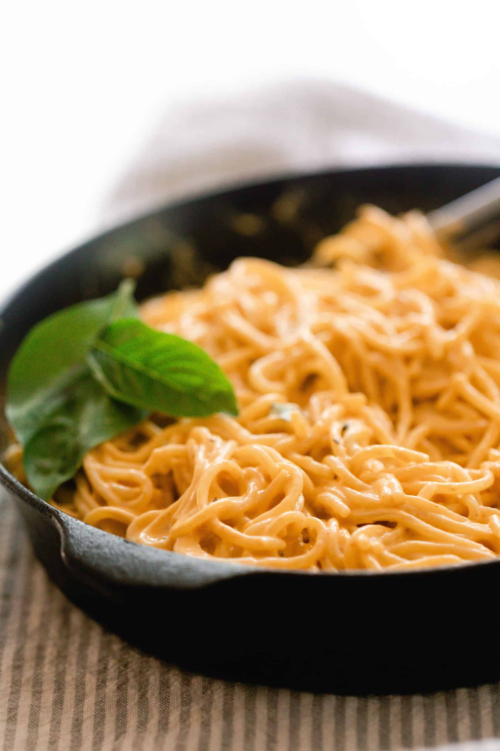 a cast iron skillet with spaghetti topped in pumpkin pasta sauce with fresh basil leaves on top