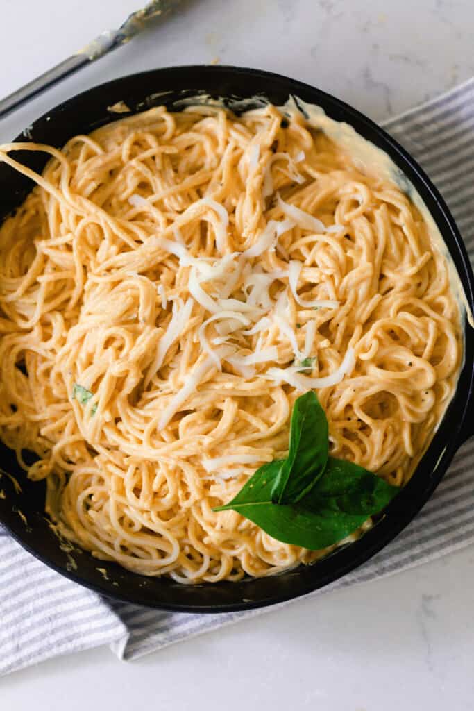 creamy pumpkin pasta sauce with spaghetti noodles mixed in in a cast iron skillet and garnished with basil. The skillet is placed on a white and gray quartz countertop