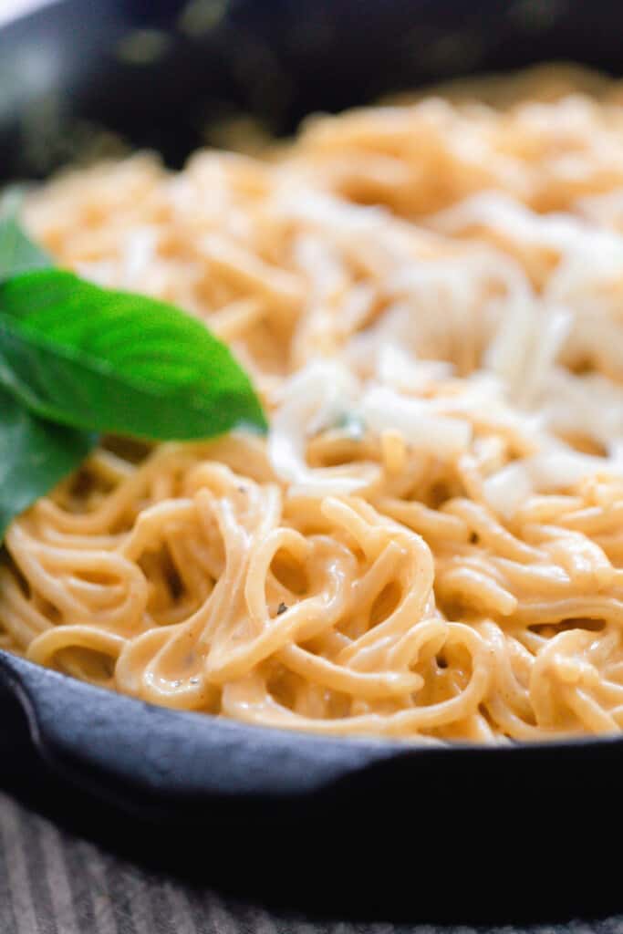 close up picture of spaghetti with creamy pumpkin sauce topped with cheese and garnished with basil in a cast iron skillet