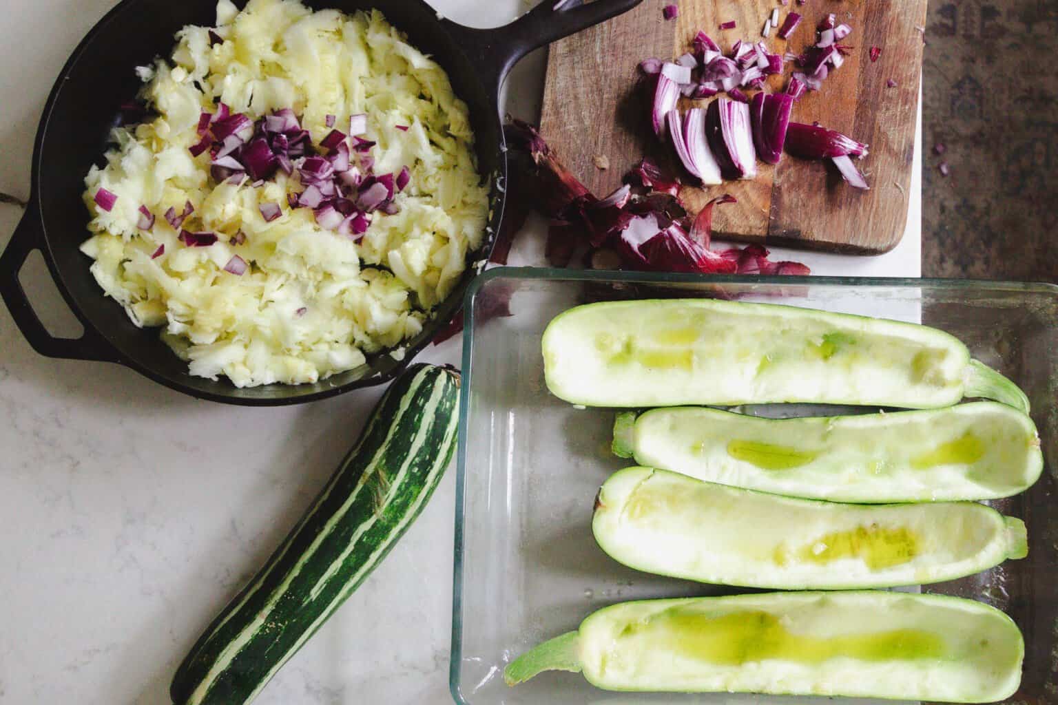 zucchini boats with a cast iron skillet full of filling to the left.