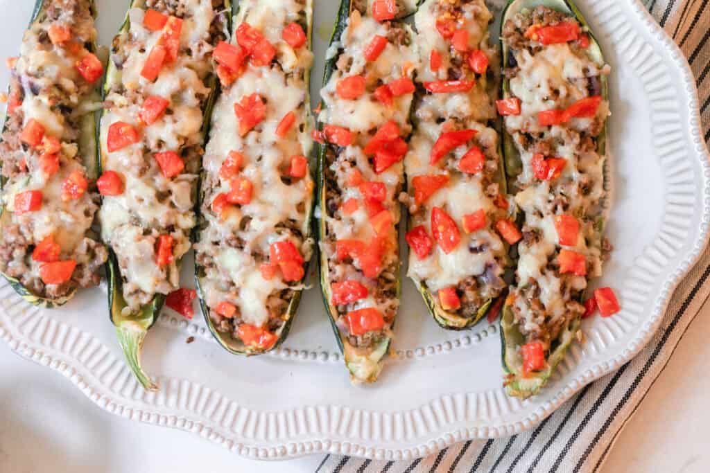six sausage zucchini boats topped with cheese and tomatoes on a white plater
