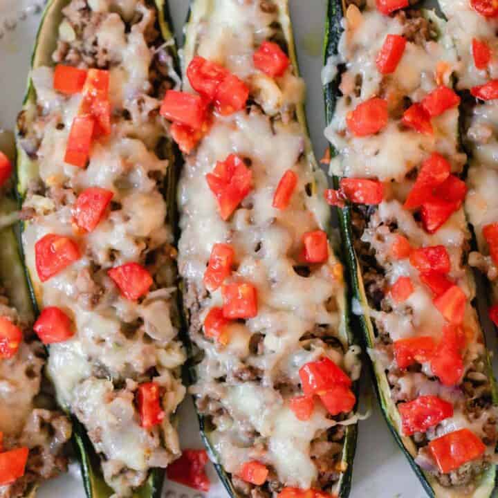 overhead photo of four sausage zucchini boats with cheese and tomatoes on a white platter
