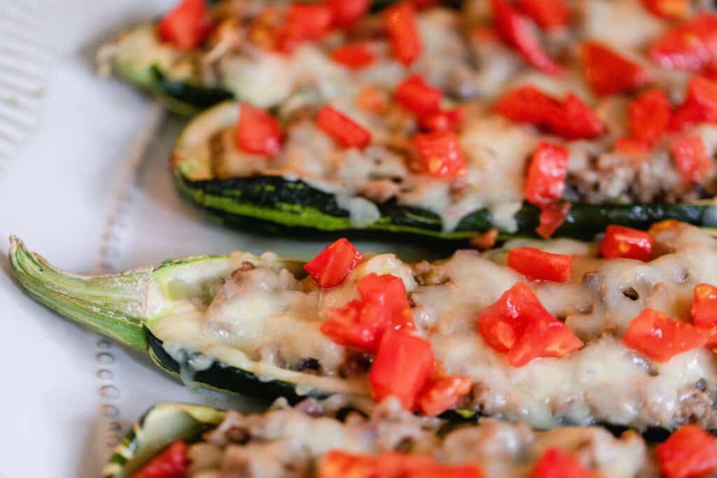 close up pictures of sausage zucchini boats topped with cheese and tomatoes