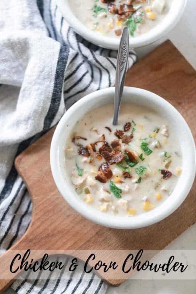 overhead photo of chicken corn chowder topped with bacon and fresh herbs on a wood cutting board on a black and white stripped towel