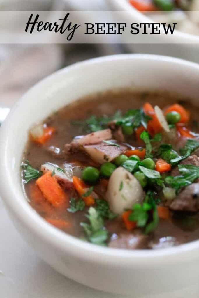 close up picture of beef stew with peas, chunks of carrots, potatoes, and tender beef in a broth and topped with herbs.