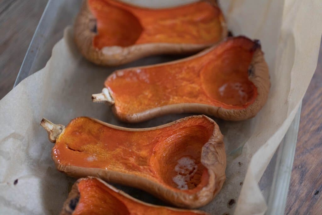 butternut squash halved with seeds scooped on an roasted on a baking dish with parchment paper