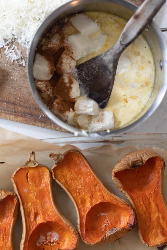 butternut squash halved and roasted on a counter with a saucepan with cream cheese, cream, sautéed onions and garlic