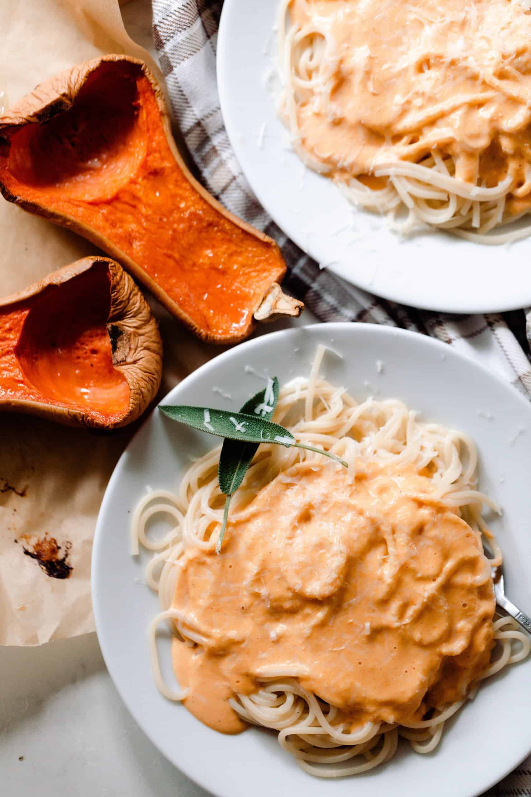 two plates our pumpkin squash pasta sauce over spaghetti with two halves of butternut squash to the side