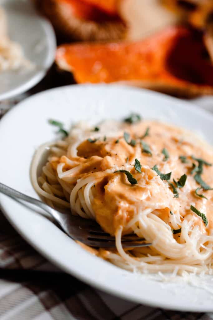 butternut squash pasta sauce poured on top of spaghetti and garnished with fresh herbs. A halved butternut squash is in the background