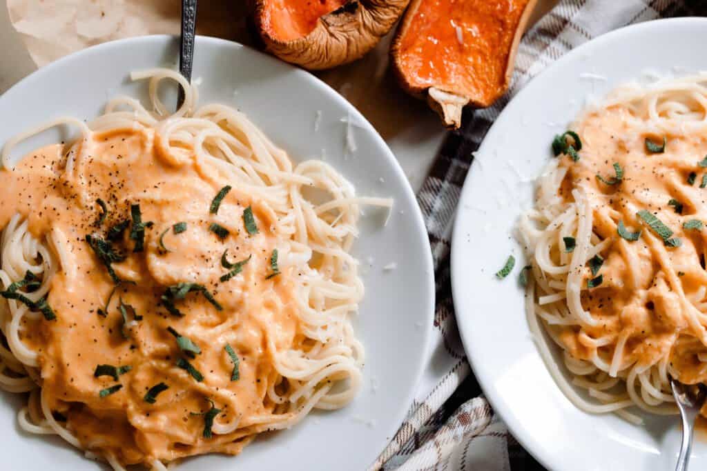 two light gray plates with spaghetti with butternut squash pasta sauce and sage over the spaghetti