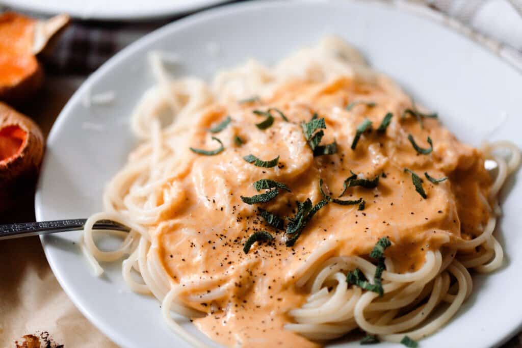 butternut squash pasta sauce on top of spaghetti on a white plate and topped with fresh sage