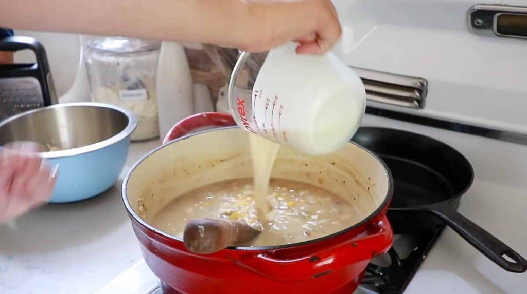 cream being added to chicken corn chowder in a red dutch oven on a white vintage stoves