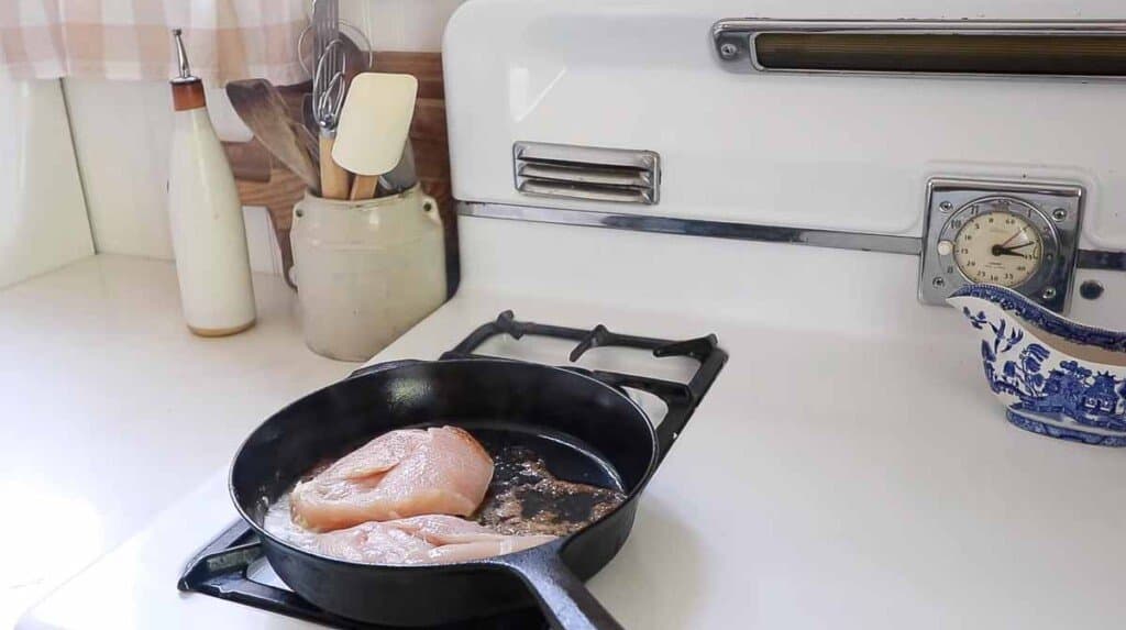 chicken being seared on a cast iron skillet with butter on a white stove