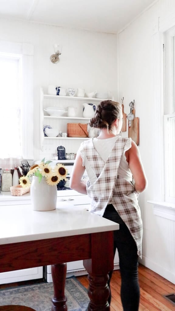 women wearing a Japanese cross-back apron in a white kitchen with a wood island with a quartz countertop