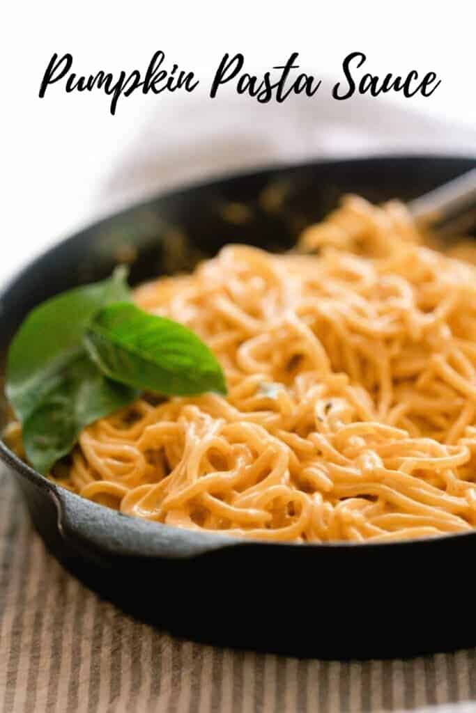 a cast iron skillet with spaghetti topped in pumpkin pasta sauce with fresh basil leaves on top