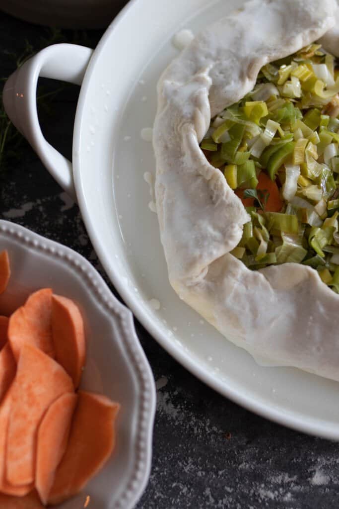 sweet potato and leek galette with the pie dough edges golden over the filling in a baking pan ready for the oven