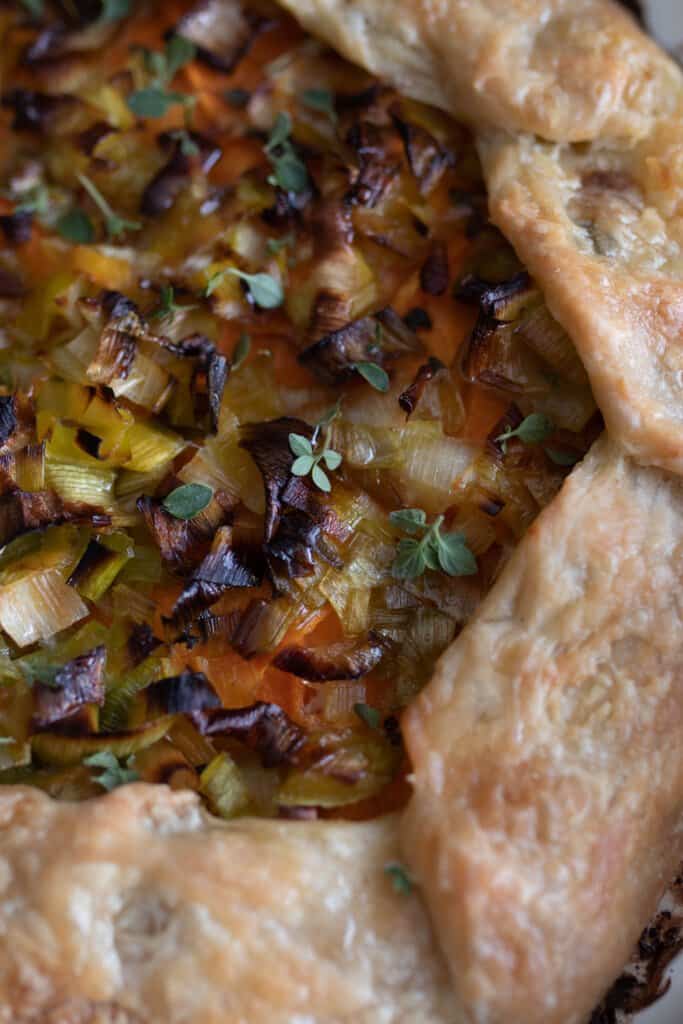 close up overhead photo of a savory sourdough galette with fresh herbs, leaks, and sweet potatoes
