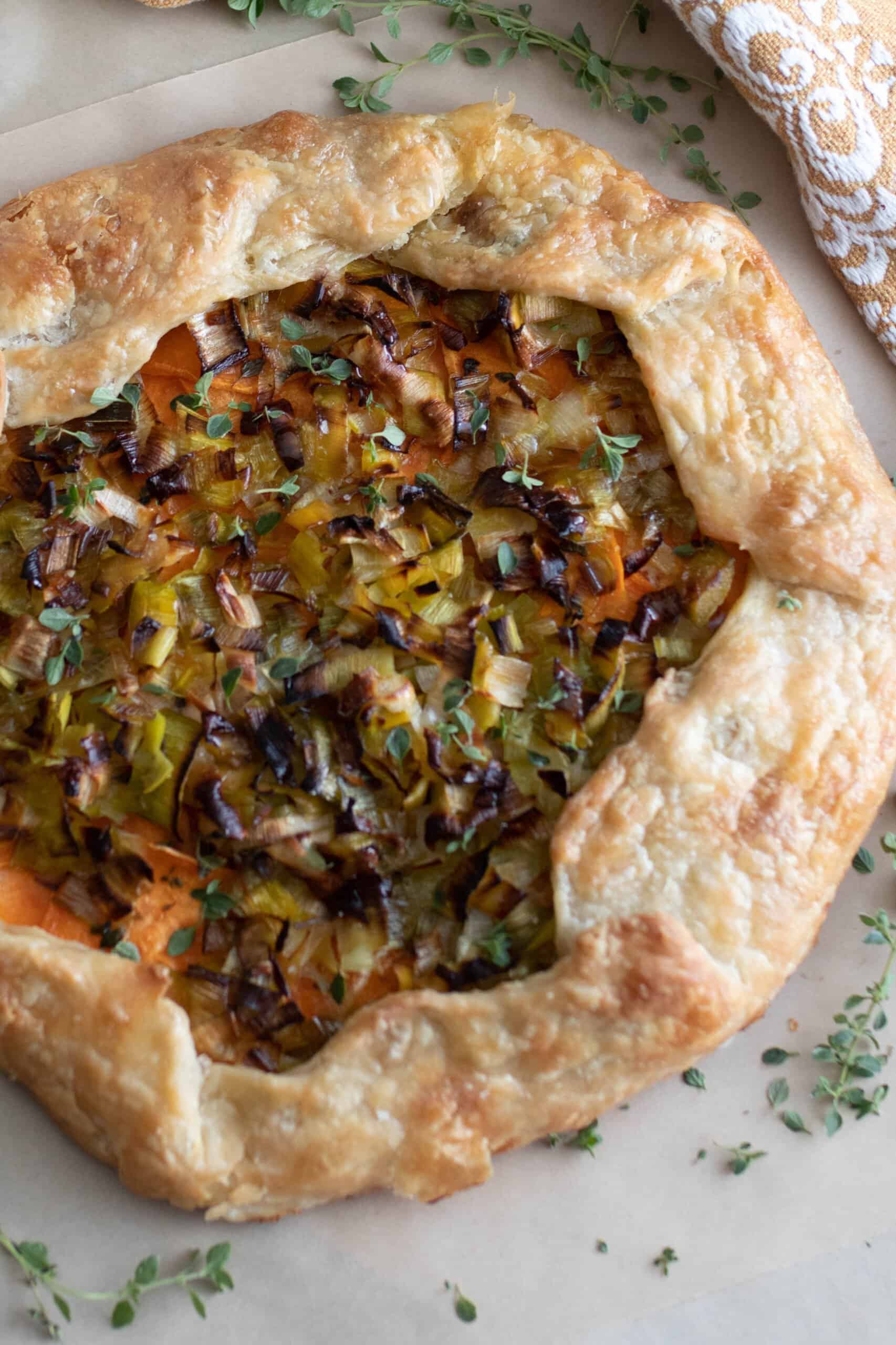 overhead photo of a sourdough galette with leeks and sweet potatoes on a marble countertop with herbs sprinkled around