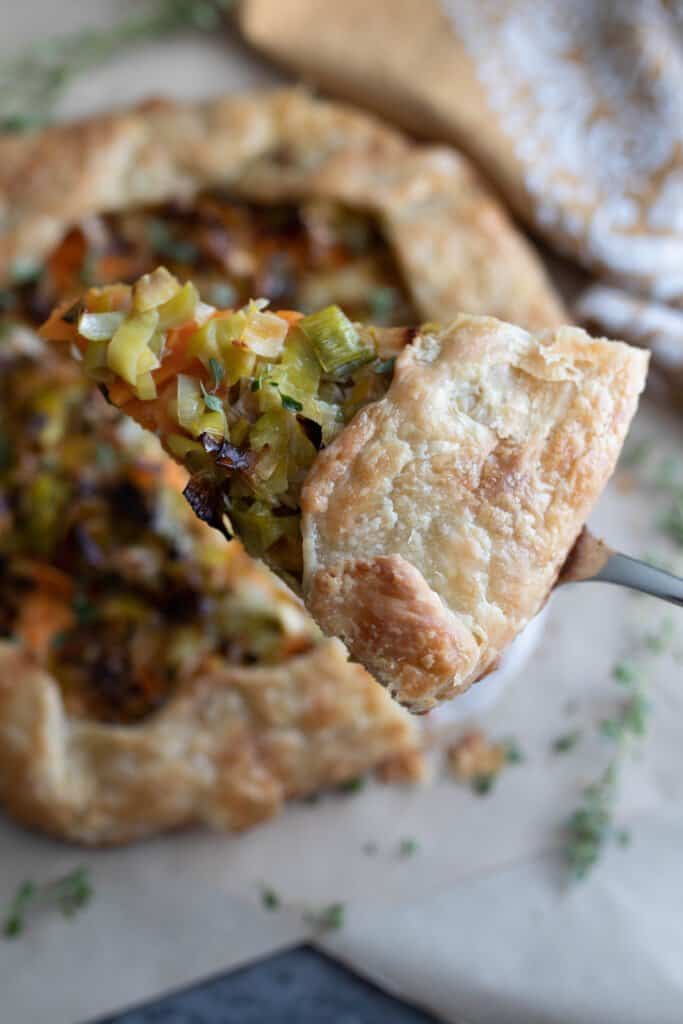 sourdough galette with sweet potatoes, leeks, goat cheese and herbs with a slice cut out and being lifted up