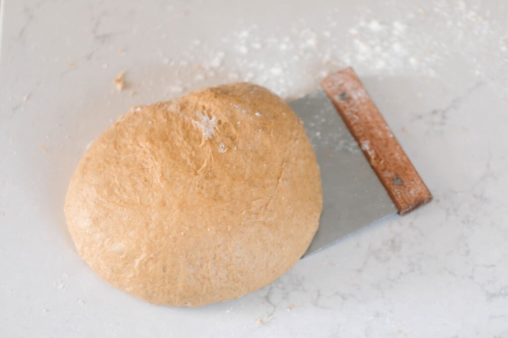 sourdough pumpkin roll dough on a white quarts countertop with a bench scraper