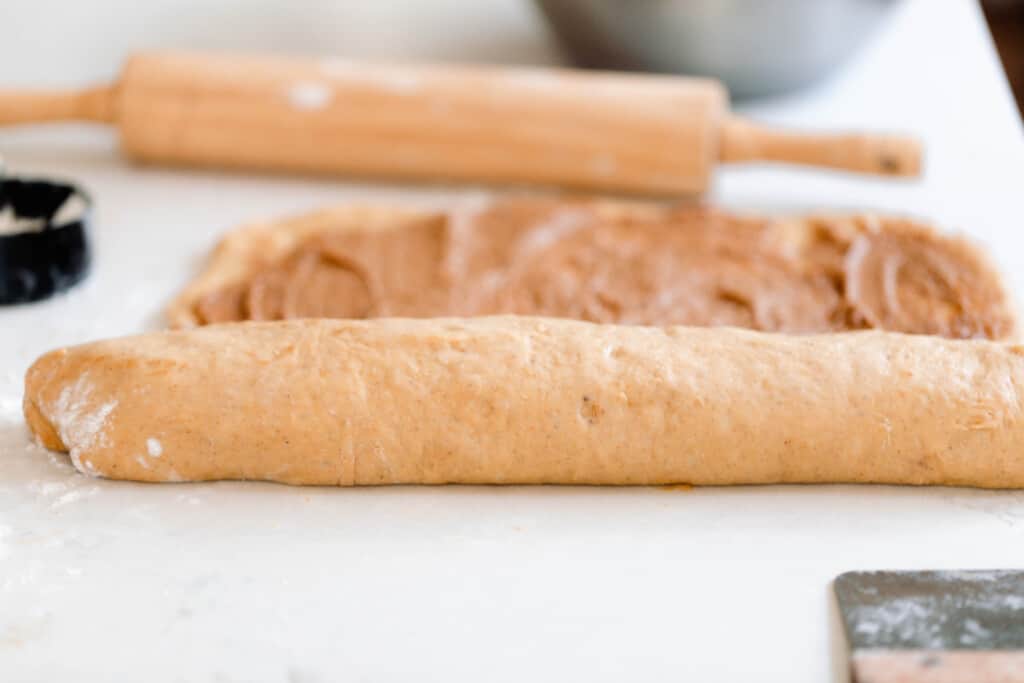 sourdough pumpkin cinnamon rolls being rolled up on a white quartz countertop