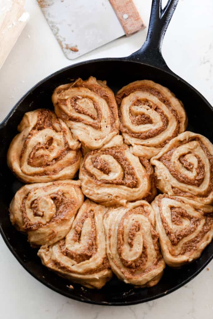 overhead photo of raw sourdough pumpkin cinnamon rolls in a cast iron skillet on a white quarts countertop