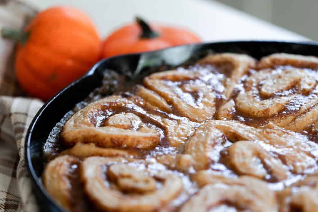 sourdough pumpkin cinnamon roll in a cast iron skillet right out of the oven with two small pumpkins in the background