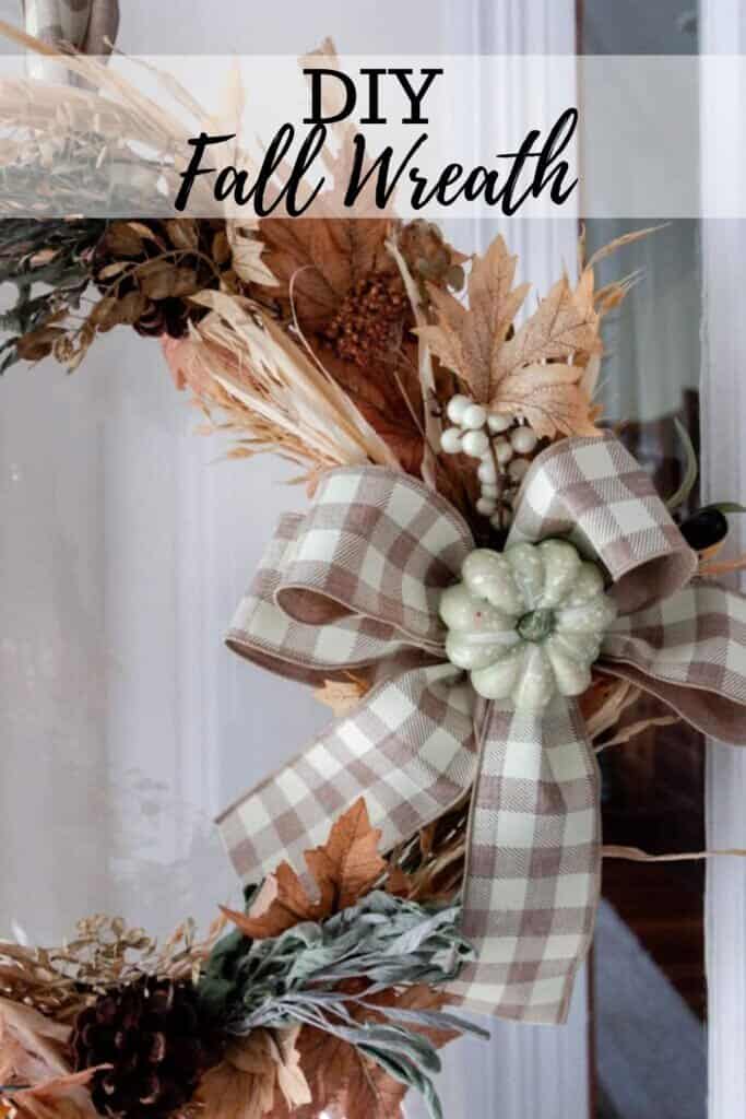 a fall wreath made with faux leaves, wheat, dried sage and tied with a tan and white checked ribbon with a light green pumpkin in the middle. 