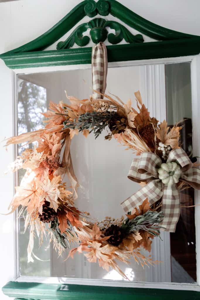 fall inspired wreath with dried leaves, and wheat with a tan and white bowl hanging out a green and white door with glass