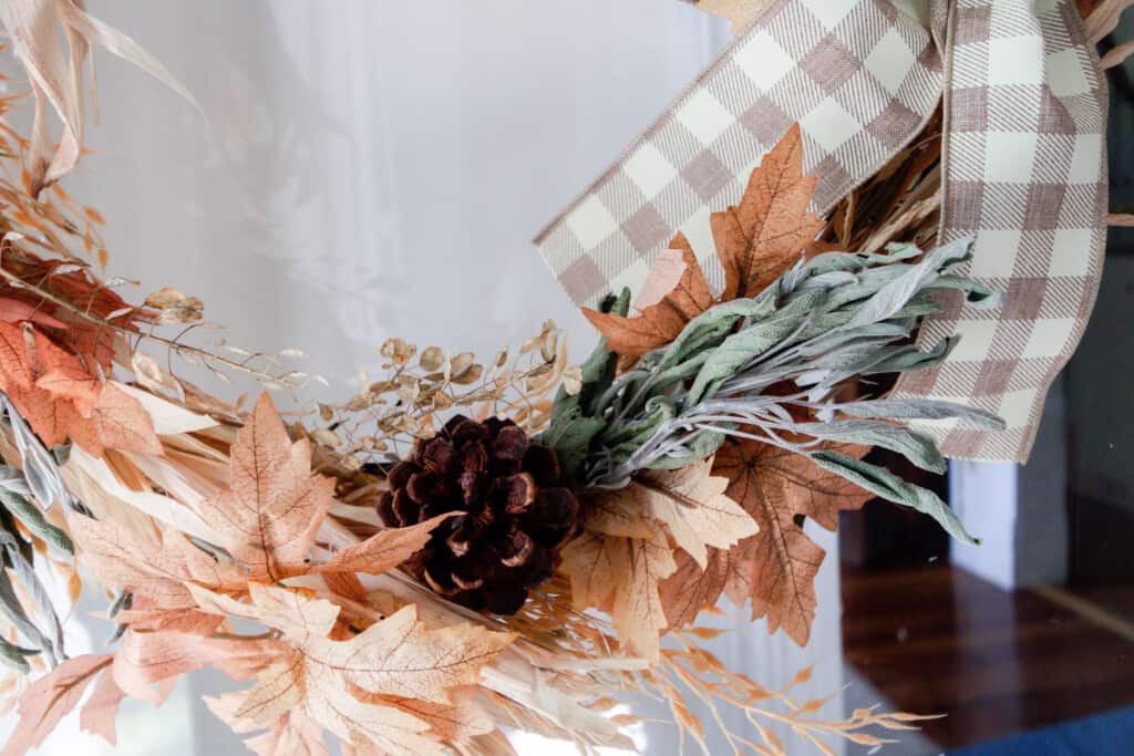 close up picture of the bottom half of a fall wreath with dried sage, pinecones, and faux maple leaves and wheat.