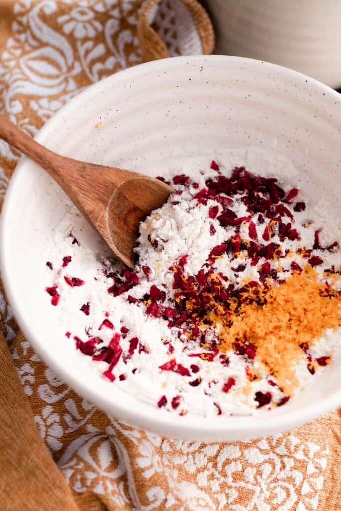 dry ingredients, dried cranberries and orange zest in a bowl with a wooden spoon on a orange and white napkin