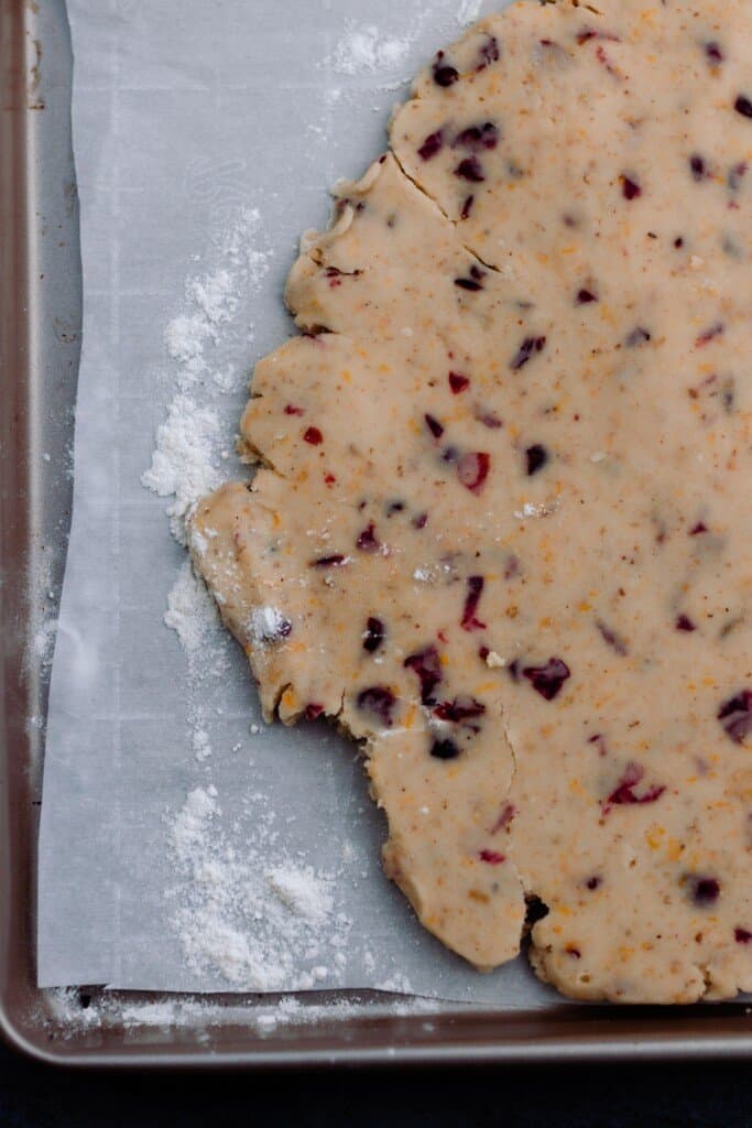 shortbread dough with orange and cranberries rolled out on parchment paper