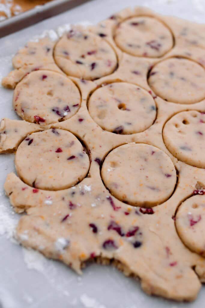orange cranberry shortbread cookie dough rolled out and cut out in circles on parchment paper