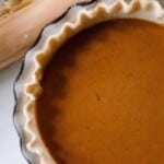a pumpkin pie on the counter with a rolling pin beside it.