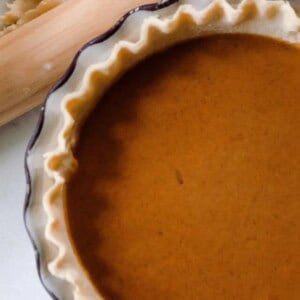 a pumpkin pie on the counter with a rolling pin beside it.