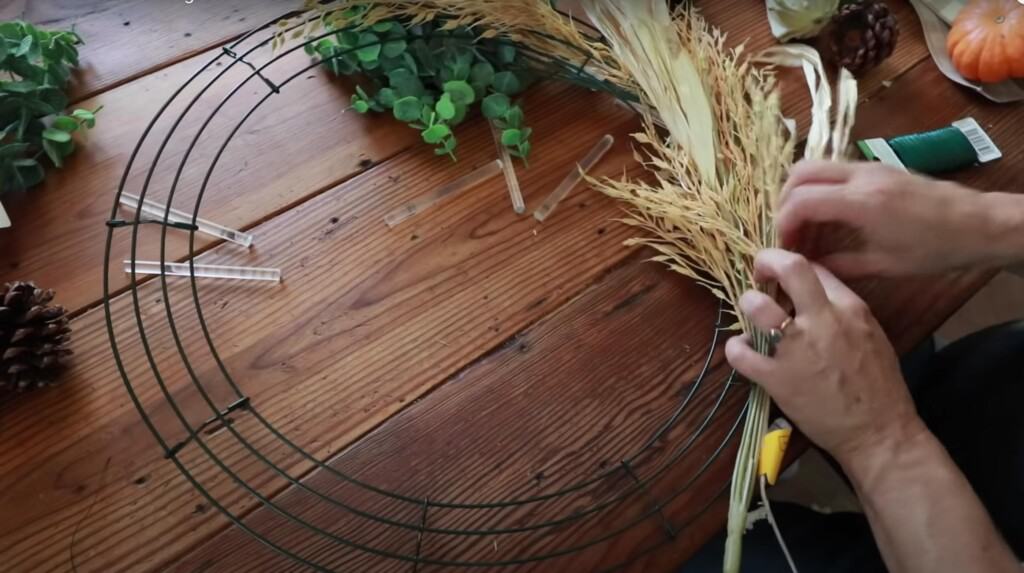 women securing faux wheat onto a wire wreath form on a wooden table