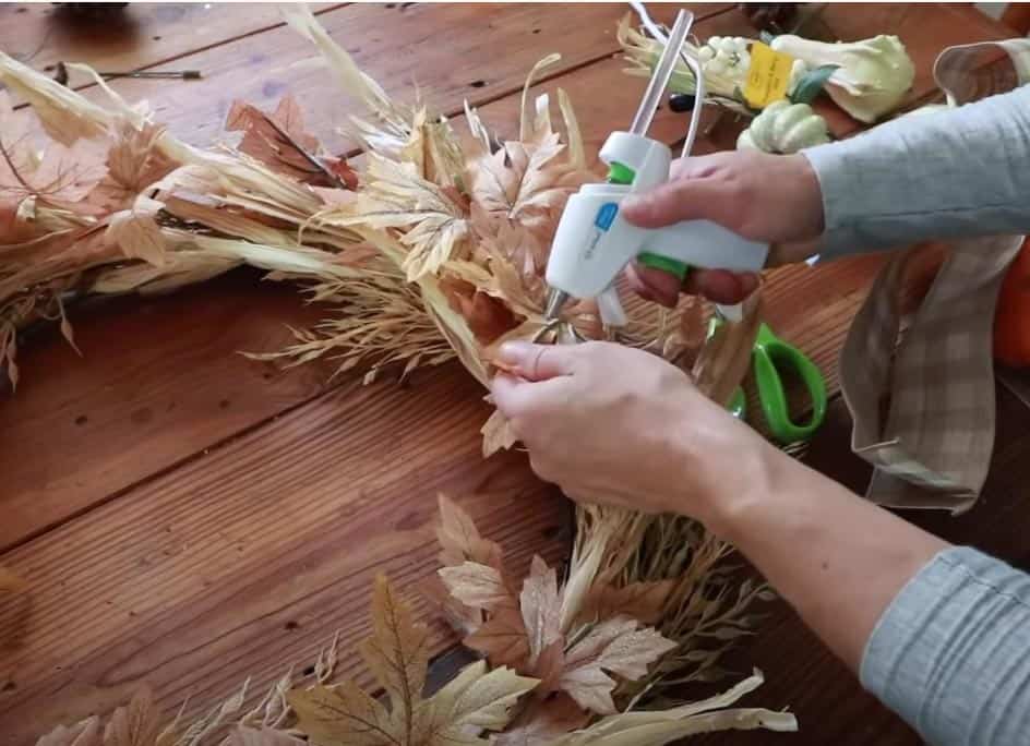 women using a hot glue gun to secure faux maple leaves onto a wreath