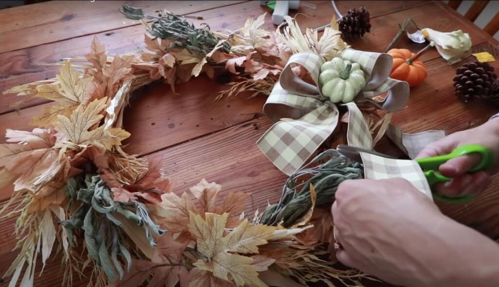 hands trimming off the tails of a ribbon bow that has been secured to a harvest wreath.