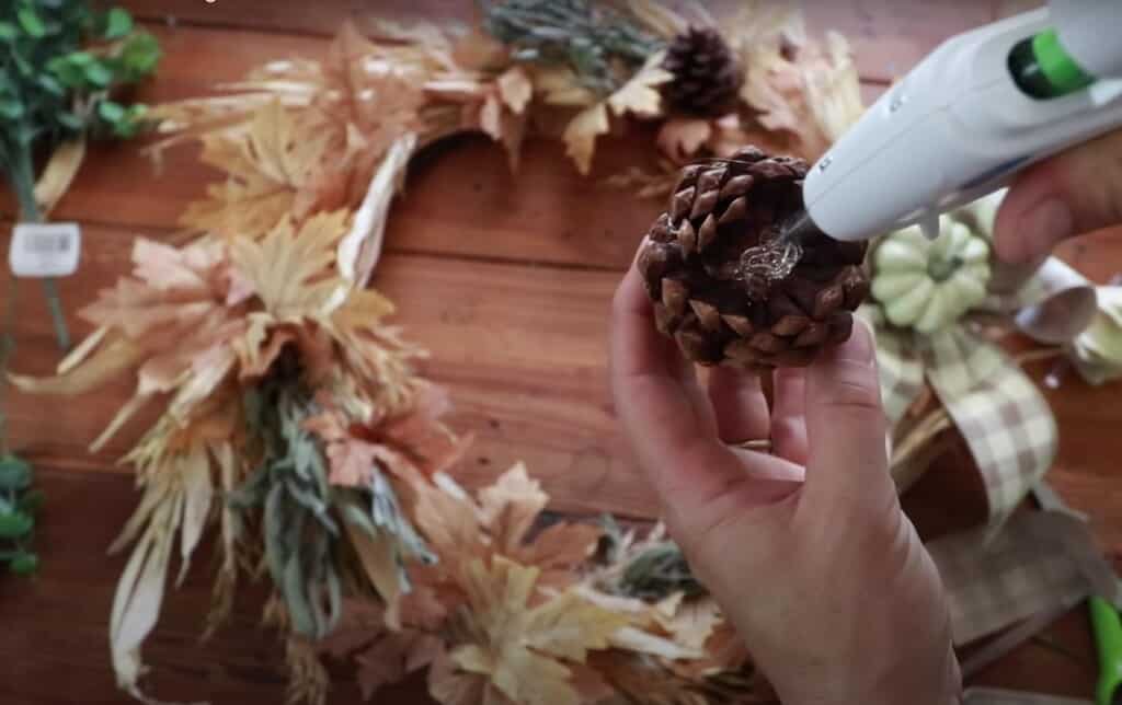 a pine cone with hot flue being added to the bottom center with a fall wreath in the background