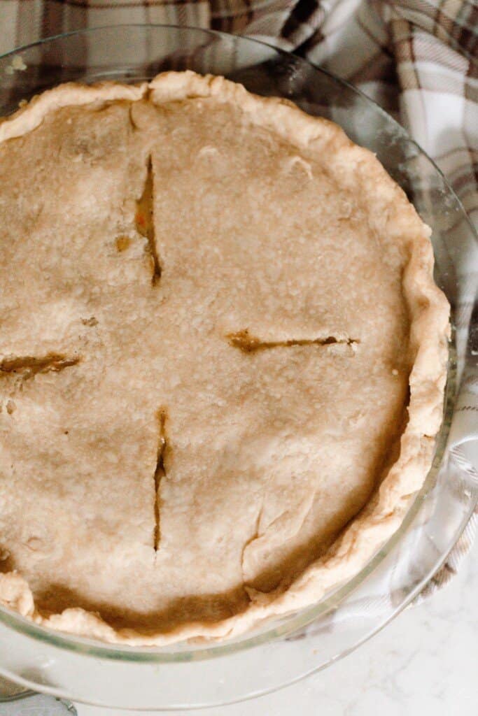 chicken pot pie with einkorn crust in a glass pie dish on a plaid cream and brown tea towel