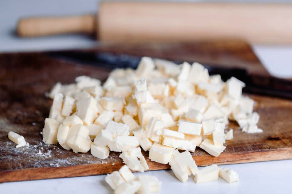 butter is diced up on a wood cutting board with a wood rolling pin in the background
