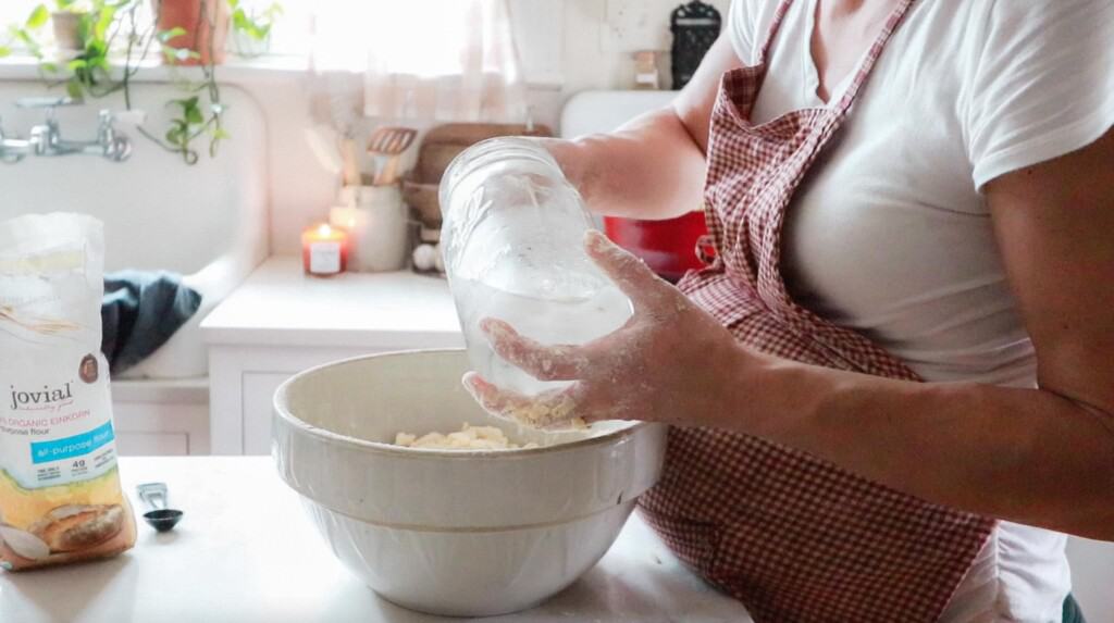 women adding ice water to a bowl of butter and flour to make a pie crust