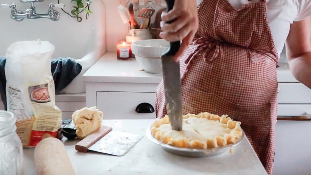 woman using a knife to cut venting slits into a pie in her white kitchen