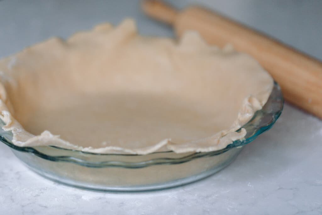 einkorn pie crust in a glass pie dish with a rolling pin behind the dish
