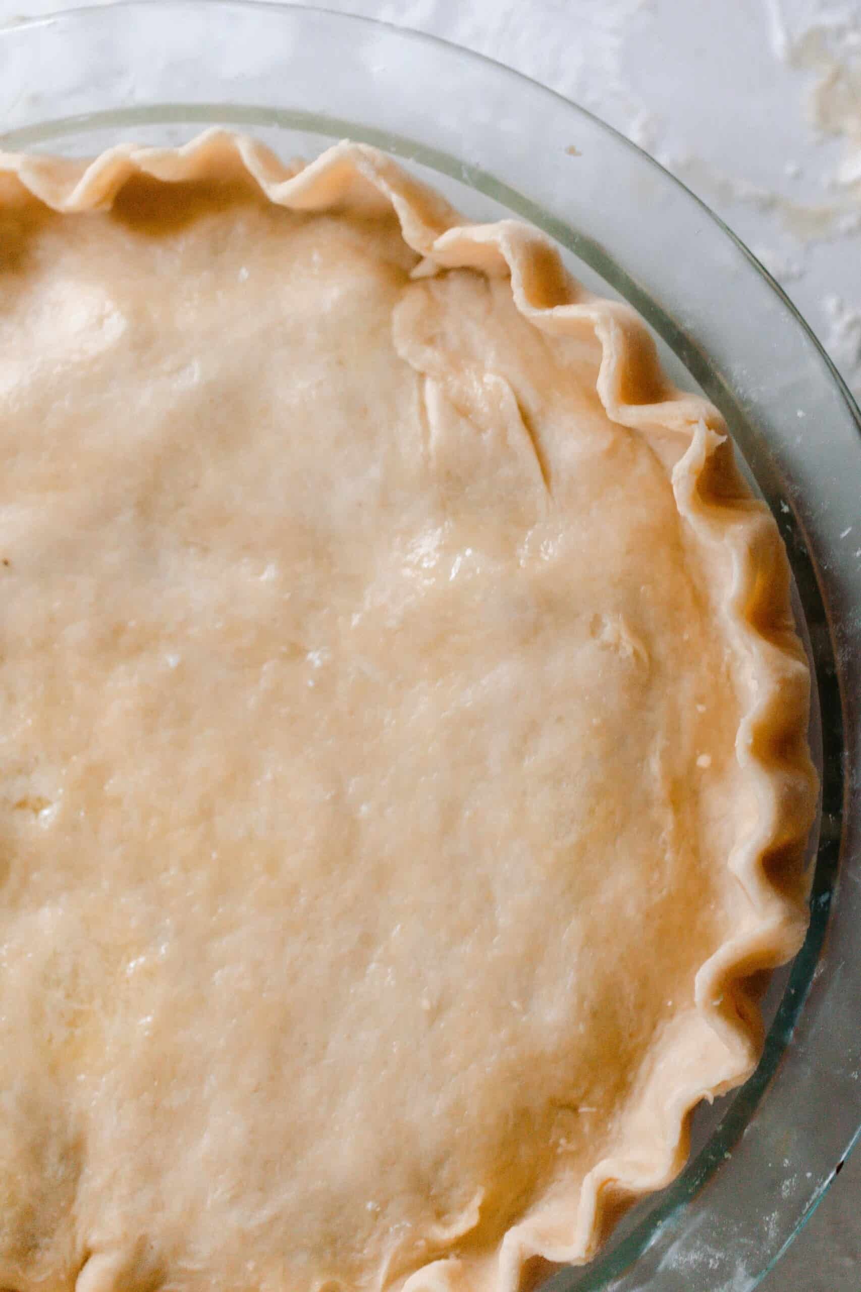 Overhead photo of einkorn pie crust used in a pie with double crust. The pie is in a glass pie dish on a white and gray quartz counter
