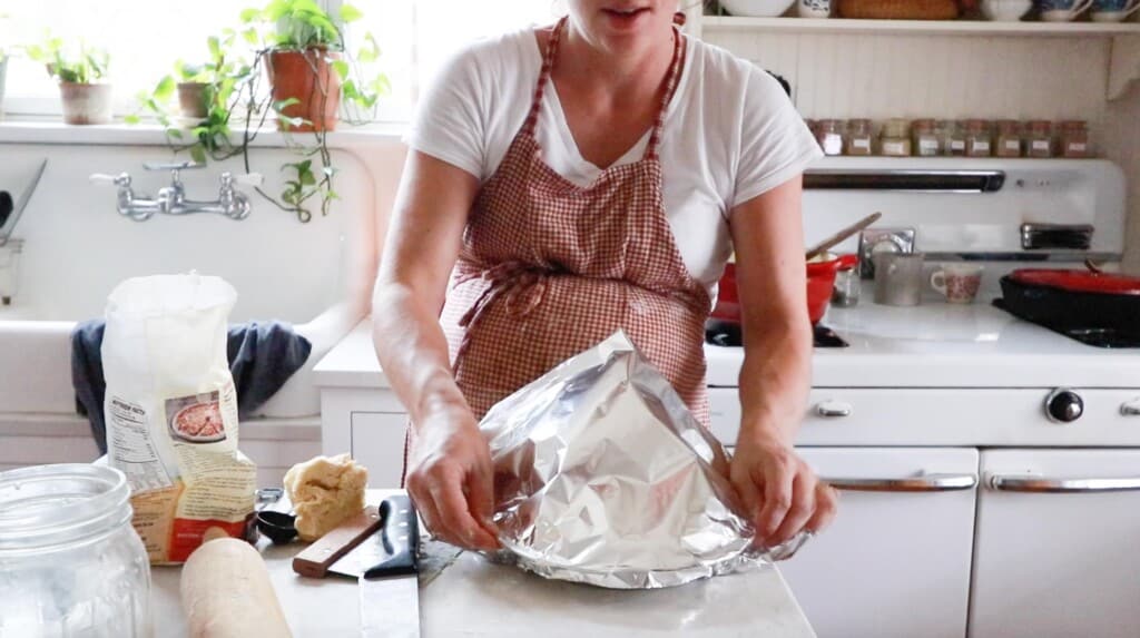 women wearing a red apron in a white kitchen placing tin foil on top of a chicken pot pie to place in the freezer